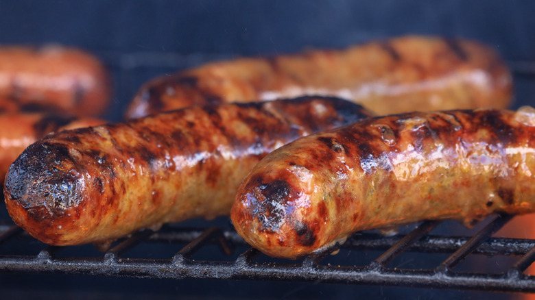 two charred brats in the foreground on a grill with three in the background