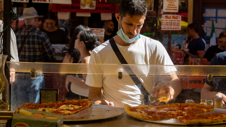 A man putting toppings on a New York style pizza