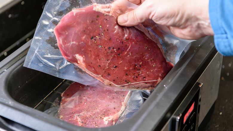 Hand putting red meat into a sous vide