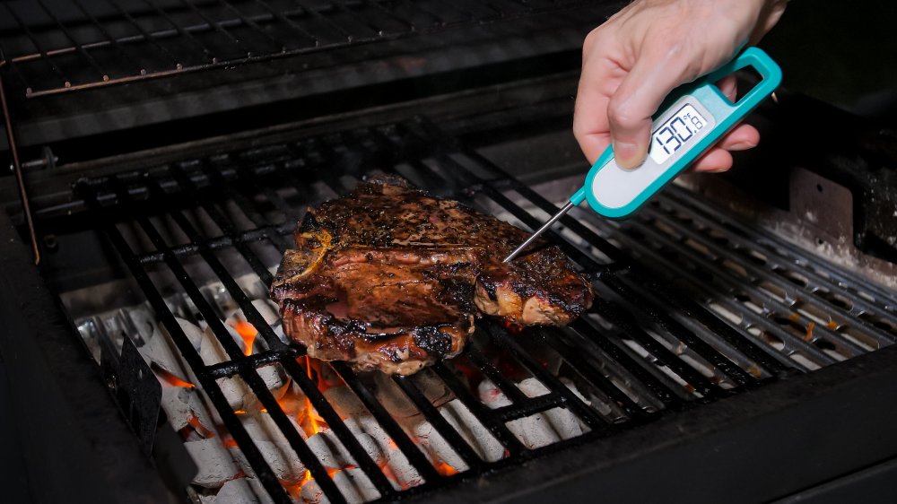hand inserting meat thermometer into steak on grill