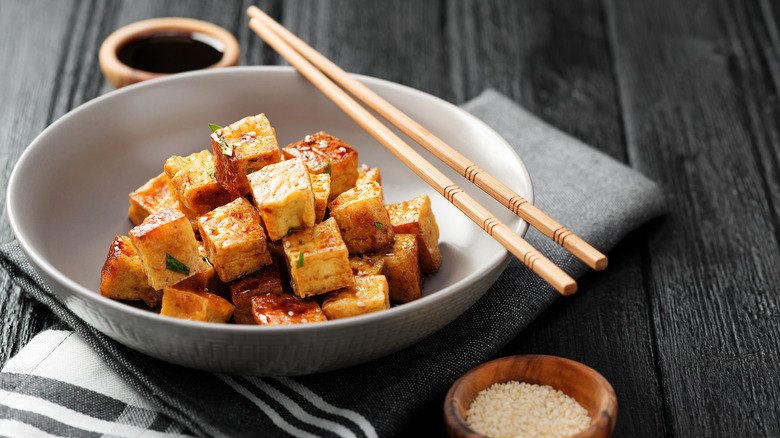 Crispy tofu with chopsticks with dipping sauce and sesame seeds