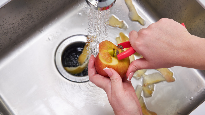 Person putting apple peel in garbage disposal