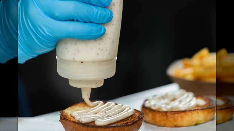 gloved hand squeezing mayonnaise onto toasted hamburger buns
