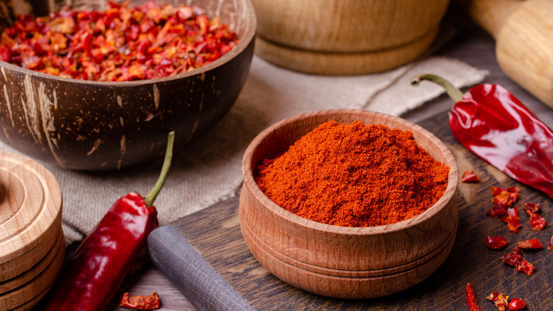 A bowl of chili powder next to red peppers 