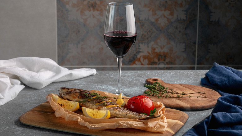 Glass of red wine on counter with cooked whole fish.