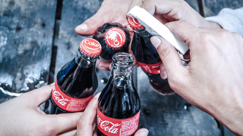 hands opening four bottles of Coca-Cola