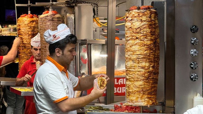 A street vendor in a kebab stand slicing meat off of a spit