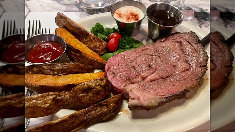A slice of prime rib served with potato wedges, ketchup, au jus, and horseradish sauce