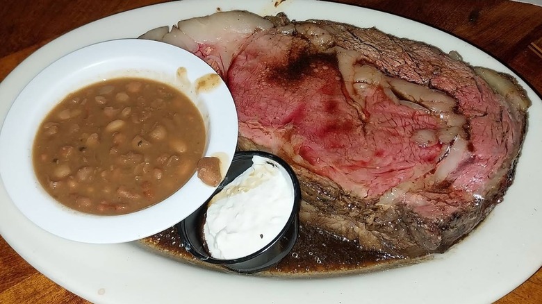 A large slice of prime rib with au jus, served with a side of baked beans and horseradish sauce