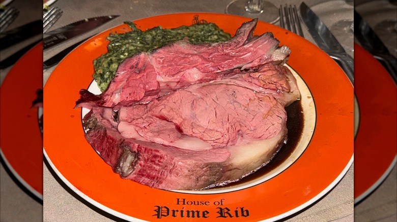 A thick slice of prime rib served in au jus with a bright green sauce next to it on an orange plate that says House of Prime Rib