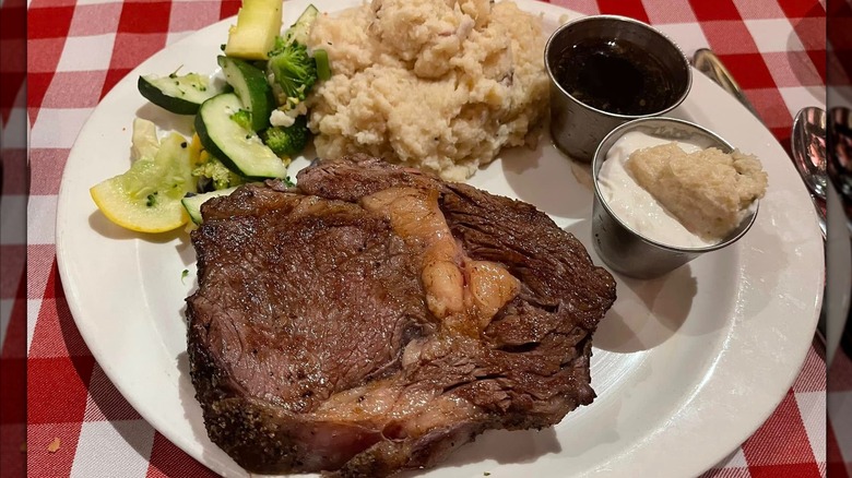 A slice of prime rib with mashed potatoes, mixed vegetables, au jus, and horseradish sauce