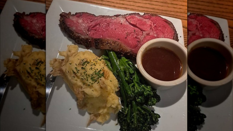 A slice of prime rib served with mashed potatoes, broccolini, and a side of au ju