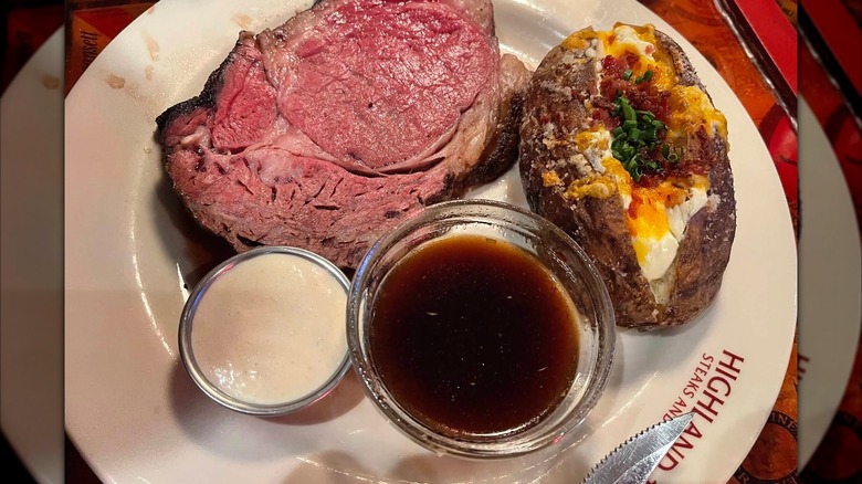 A slice of prime rib with au jus and horseradish sauce, served with a loaded baked potato