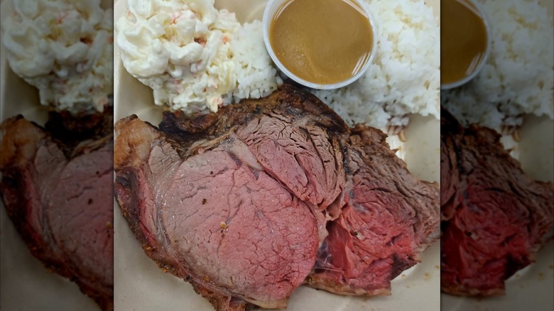 Sliced prime rib with white rice, macaroni salad, and gravy in a takeout container