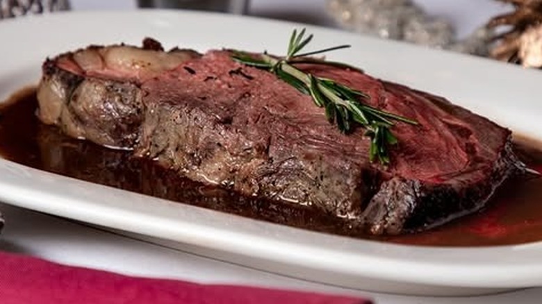 A slice of prime rib on a white plate with rosemary