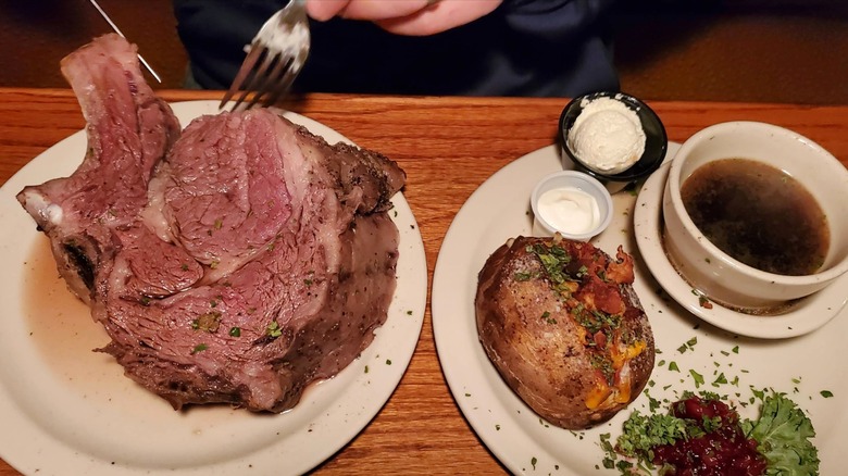 A bone-in prime rib with au jus, a baked potato, and horseradish