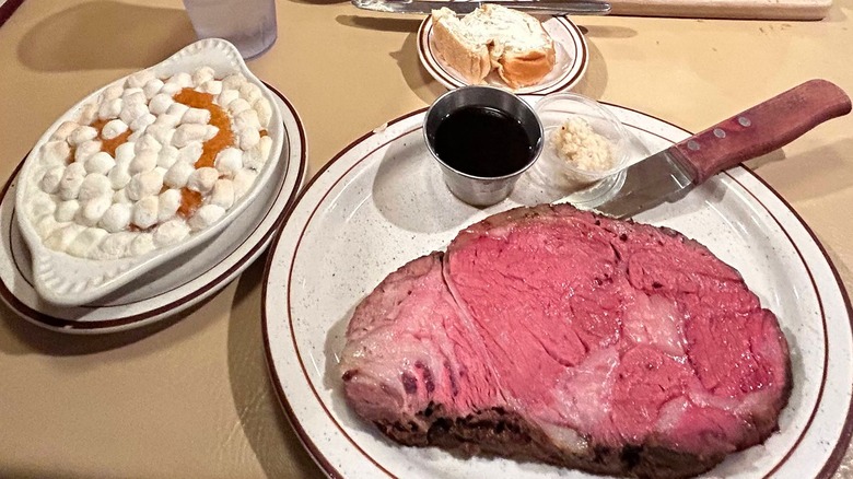 A slice of prime rib served with au jus and horseradish, with a side of sweet potato casserole topped with marshmallows