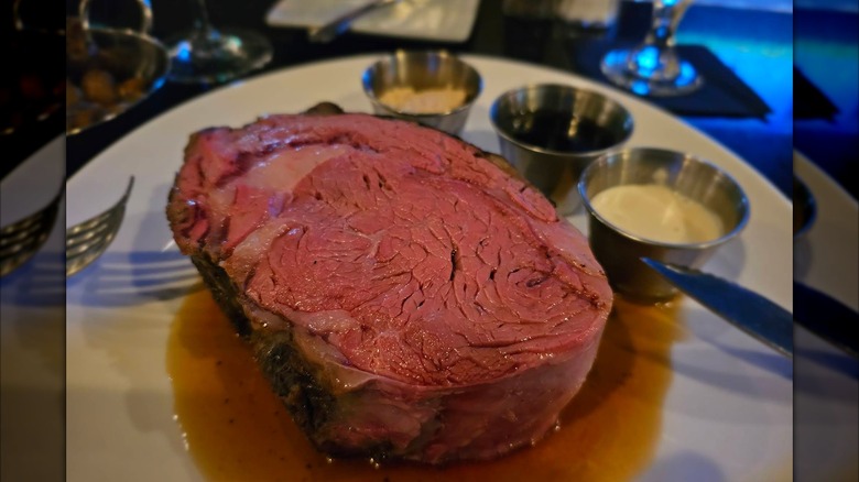 A slice of prime rib in au jus with three different sauces