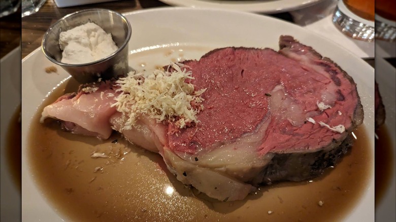 A piece of prime rib on a plate with au jus and a side of horseradish sauce