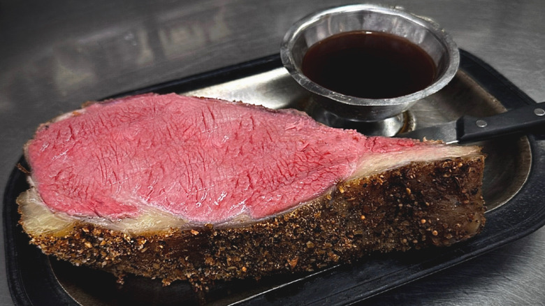 A thick slice of pepper-crusted prime rib with a side of au jus