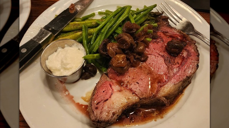 A piece of prime rib with horseradish sauce, asparagus, and mushrooms