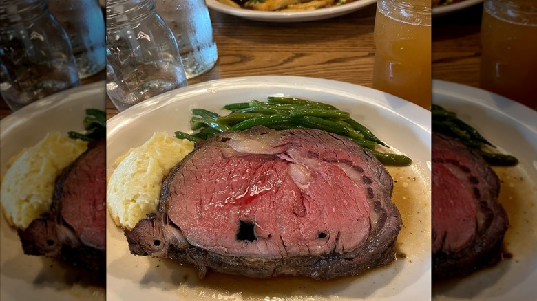 A piece of prime rib on a plate with mashed potatos and green beans