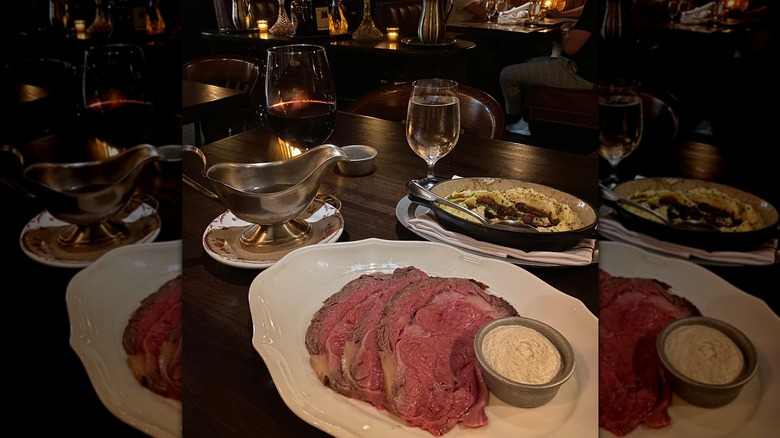 Thin slices of prime rib with a side of horseradish sauce on a white plate with a serving dish of au jus and a side dish of mashed potatoes