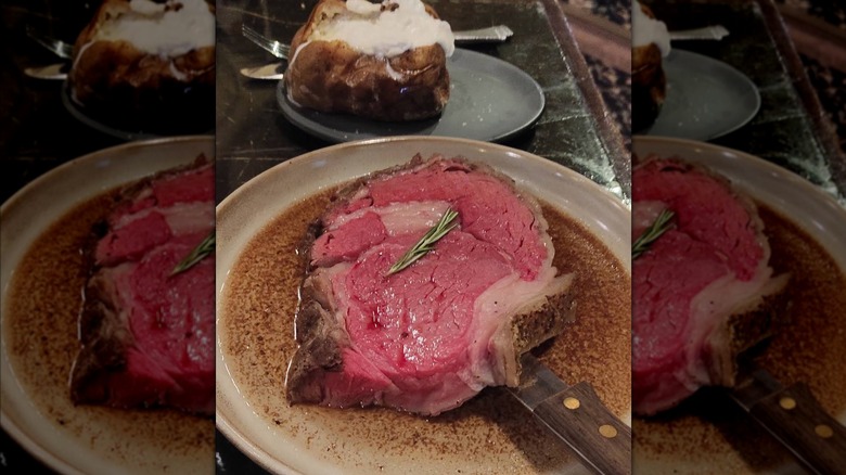 A slice of prime rib served in its own au jus and a baked potato as a side