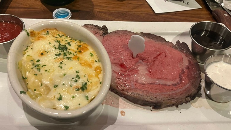 A slice of prime rib with au jus and horseradish sauce on the side, along with a creamy side dish