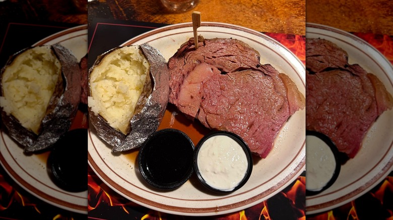 A slice of prime rib served with au jus, horseradish sauce, and a baked potato