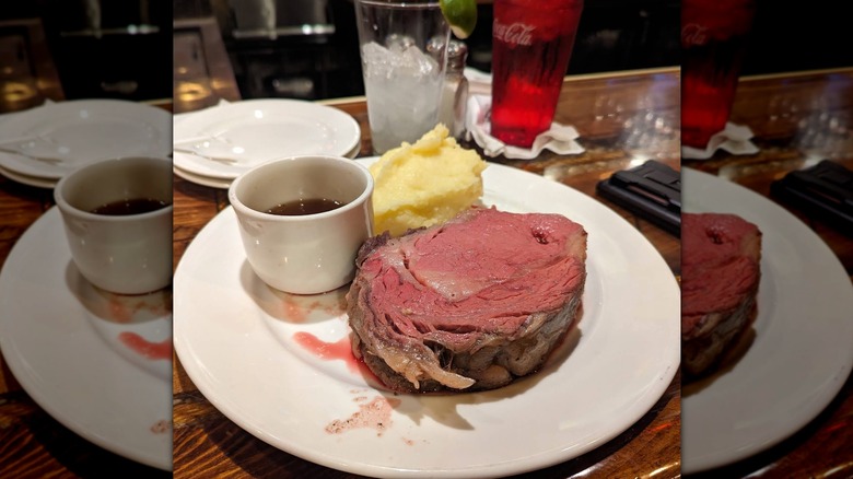 A pink slab of prime rib served with au jus and mashed potatoes