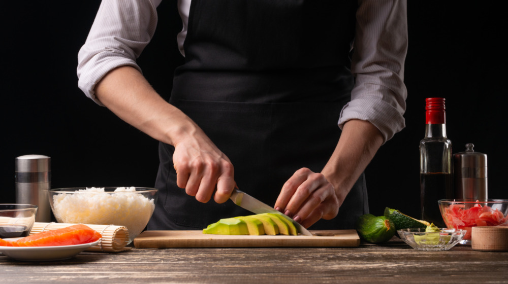 Chef cutting avocados with sushi ingredients nearby