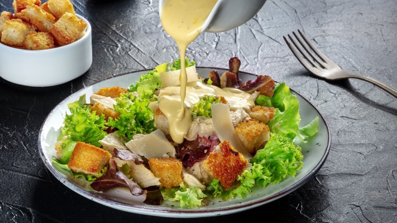 Dressing poured over a classic Caesar salad