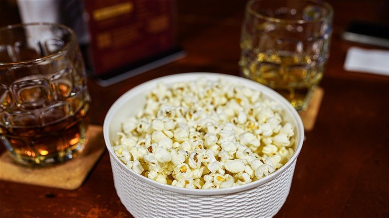 Bowl of popcorn in front of two glasses of whiskey.