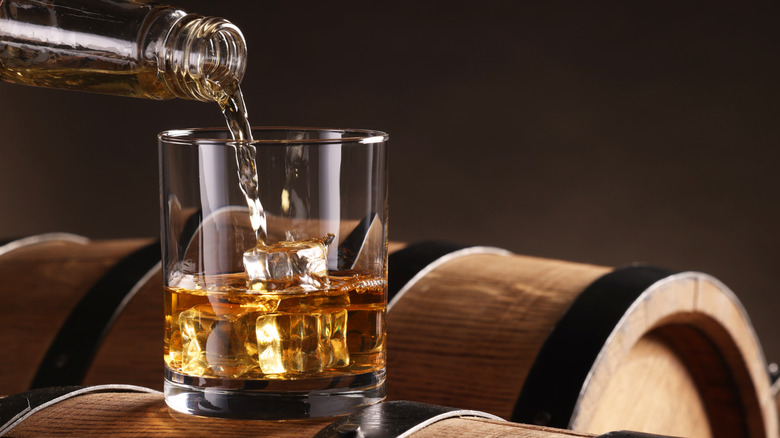 Bourbon being poured into glass placed on barrels