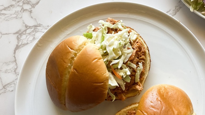 Two barbecue chicken sandwiches on white plates with coleslaw