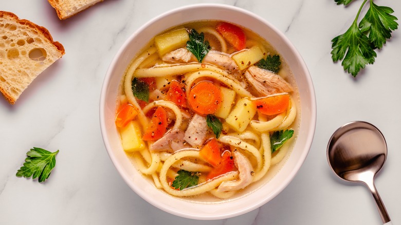 Bowl of chicken noodle soup with carrots, chicken, and parsley