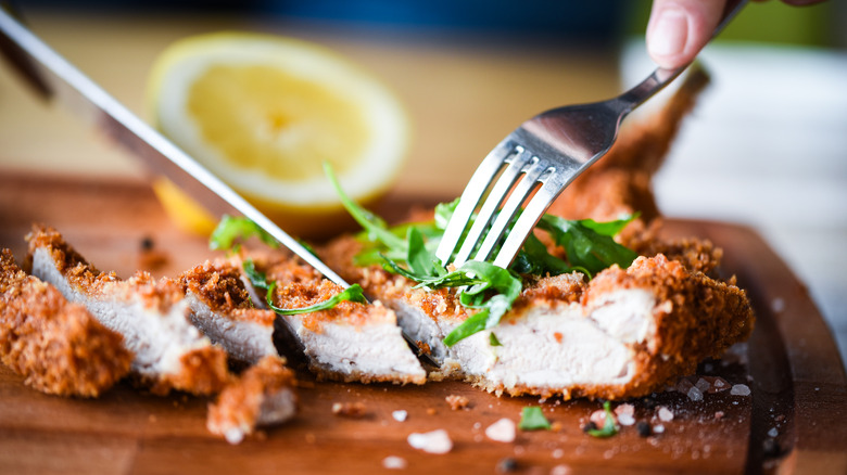 Knife and fork cutting chicken schnitzel