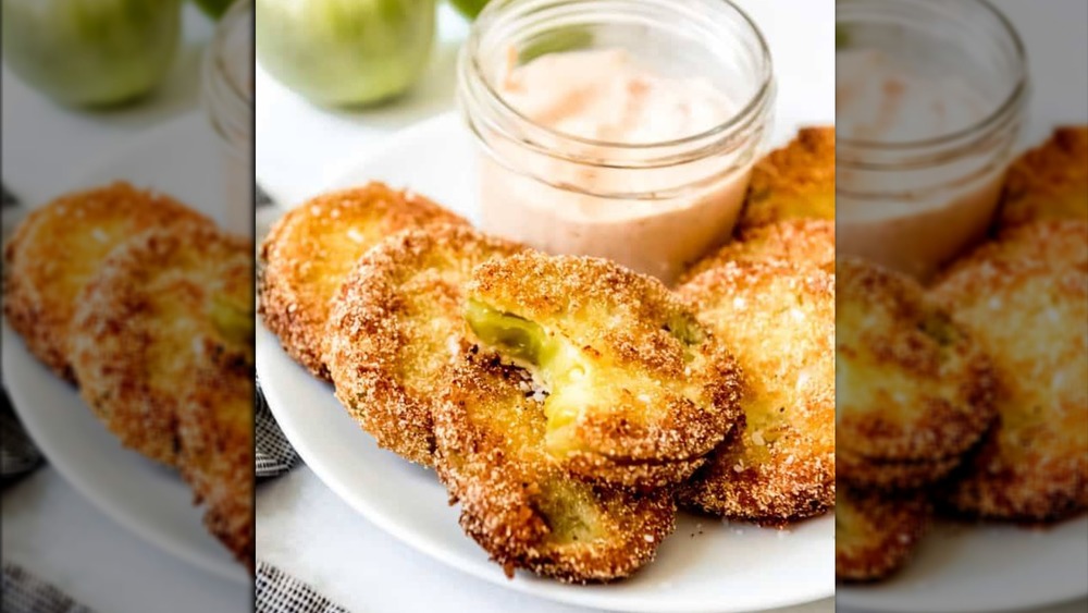 Slices of fried green tomatoes on a white plate and a small cup of dipping sauce.