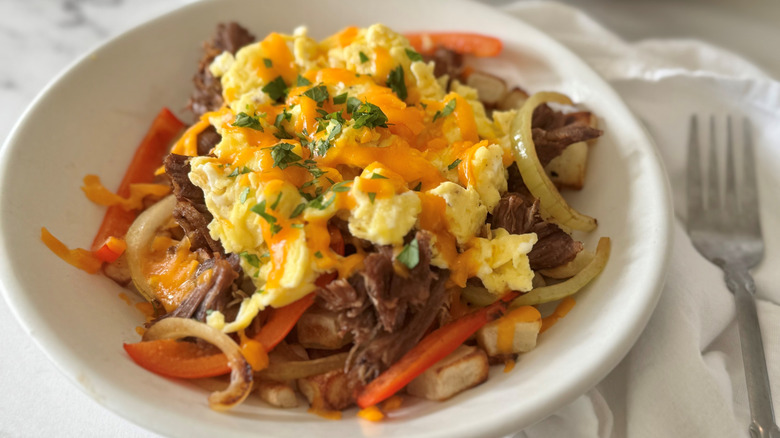 scrambled eggs, meat, vegetables, and cheese in a white bowl