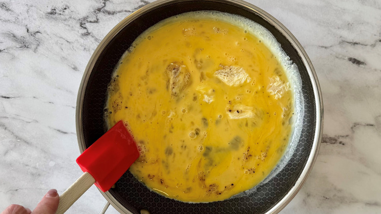 hand holding a rubber spatula in a pan of raw beaten eggs