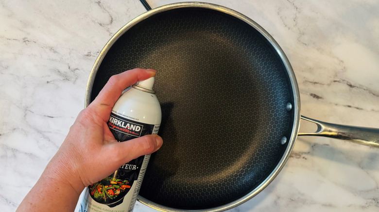 hand holding a spray can over a black frying pan