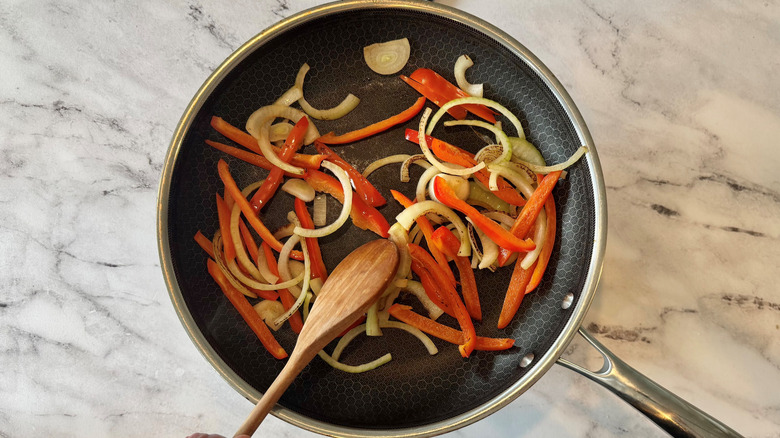 hand holding a wooden spoon in a pan of vegetables