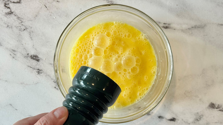 hand holding a green pepper grinder over a bowl of raw eggs