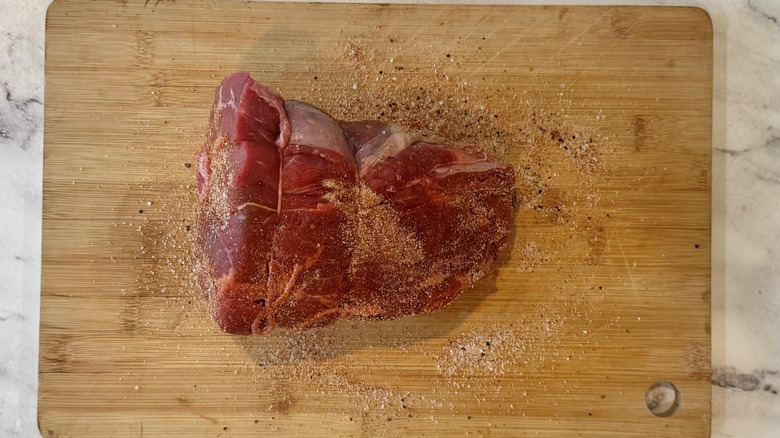 seasoned and string-wrapped raw chuck roast on a wooden board