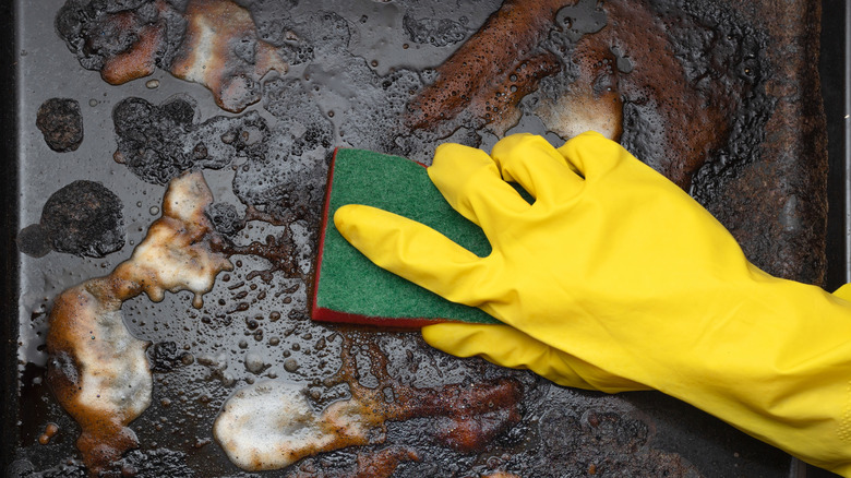 Gloved hand scrubbing dirty baking sheets