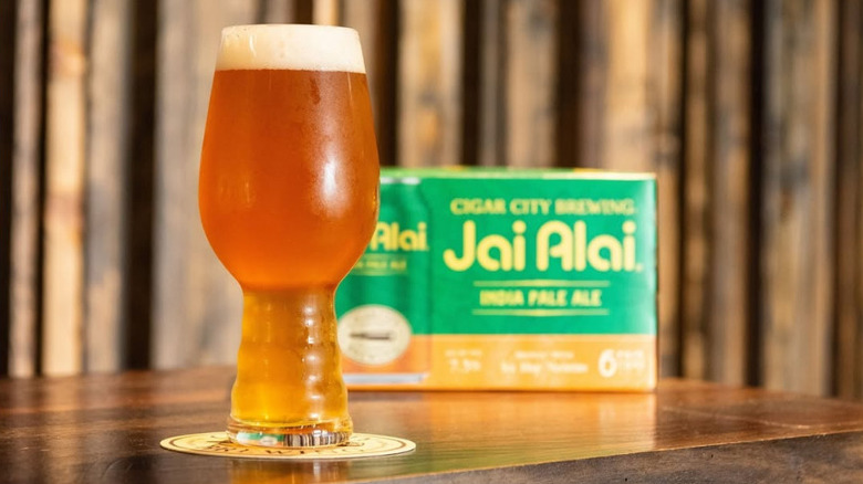 a full IPA glass in front of a box of Jai Alai cans
