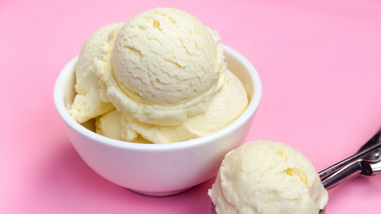 Scoop and bowl of vanilla ice cream on pink background