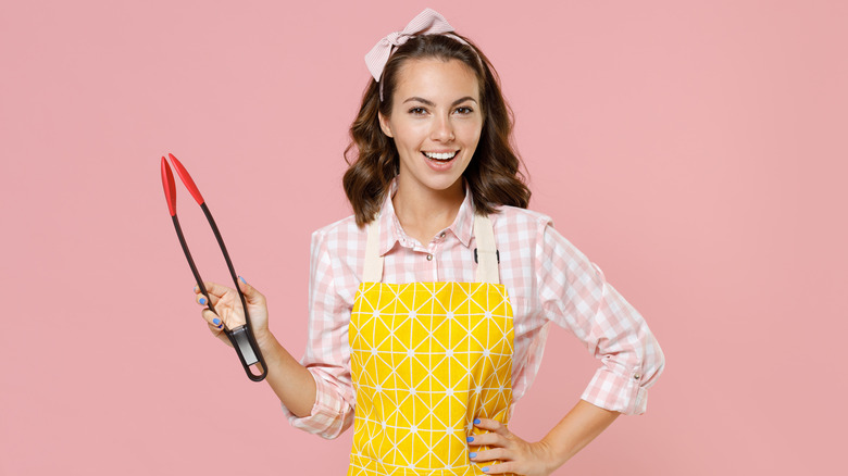 woman in apron holding kitchen tongs and smiling