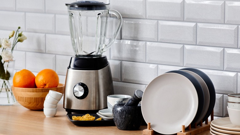 Blender on counter top with bowl of oranges and dishes